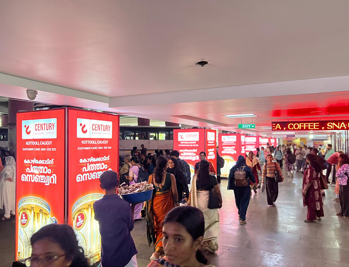 Row of backlit Century Wedding Centre light boxes along the Calicut bus stand concourse